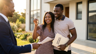 Happy Nigerian couple holding house keys and mortgage documents in front of their new home